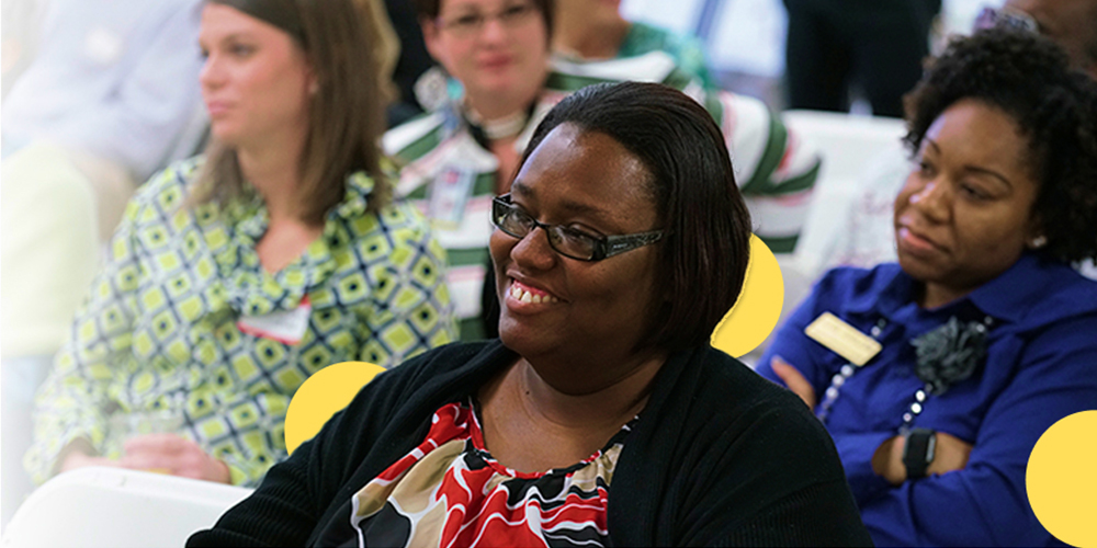 Women smiling on an event with a group of people on the background