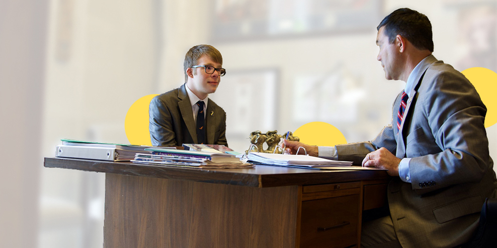 A young person sitting on desk talking with a older man in a legal office 